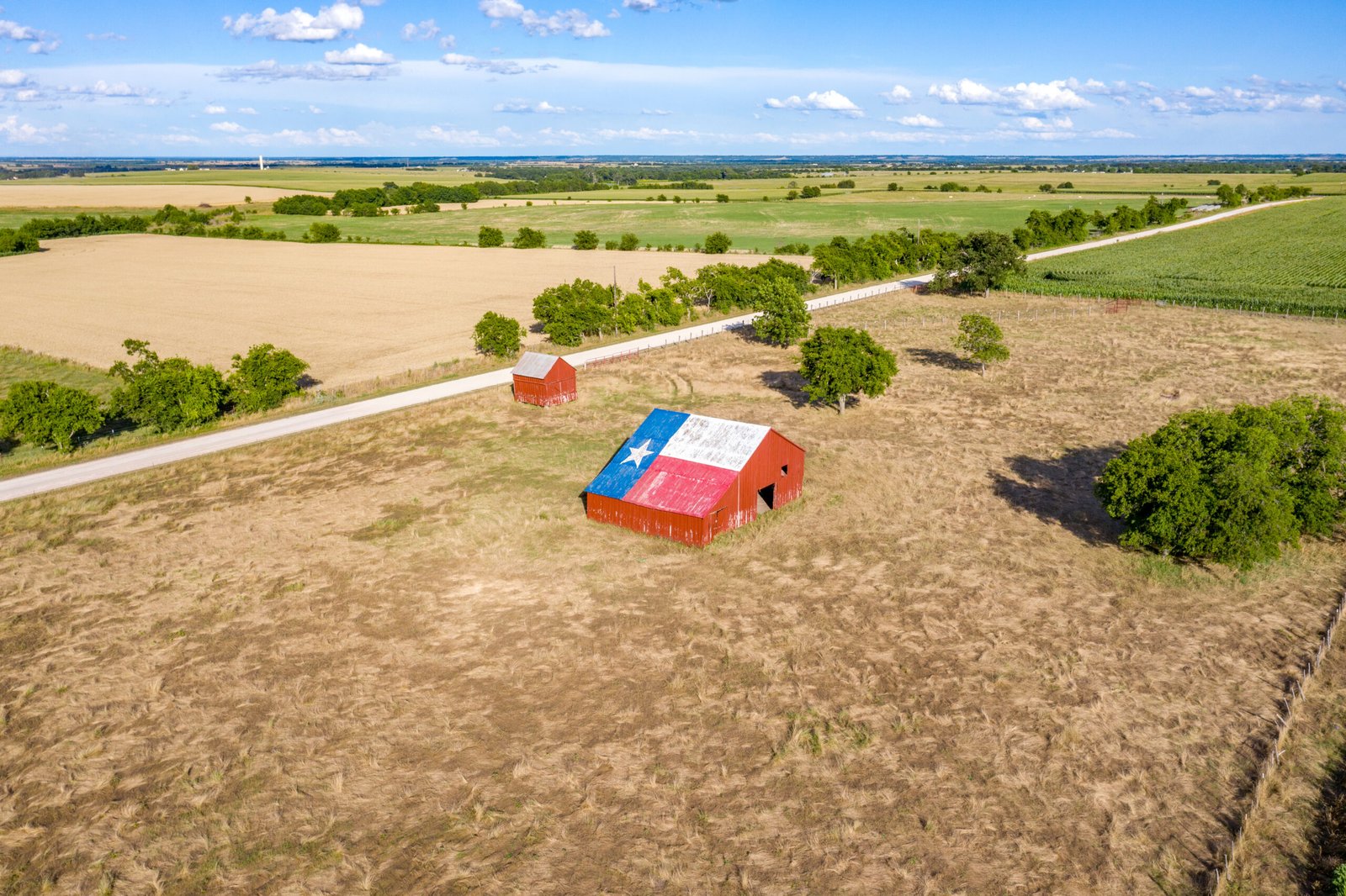 An abandoned old barn with the symbol of Texas painted on the roof sits in a rural area of the state, framed by farmland.